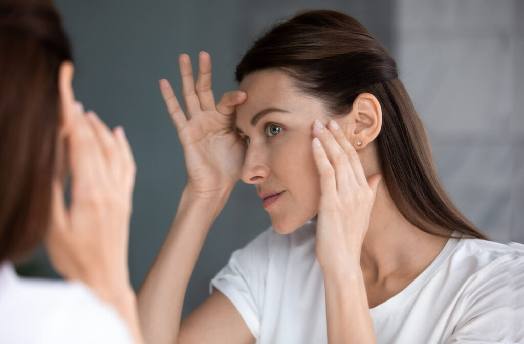 A person inspects their fine lines and under-eye wrinkles in the mirror.
