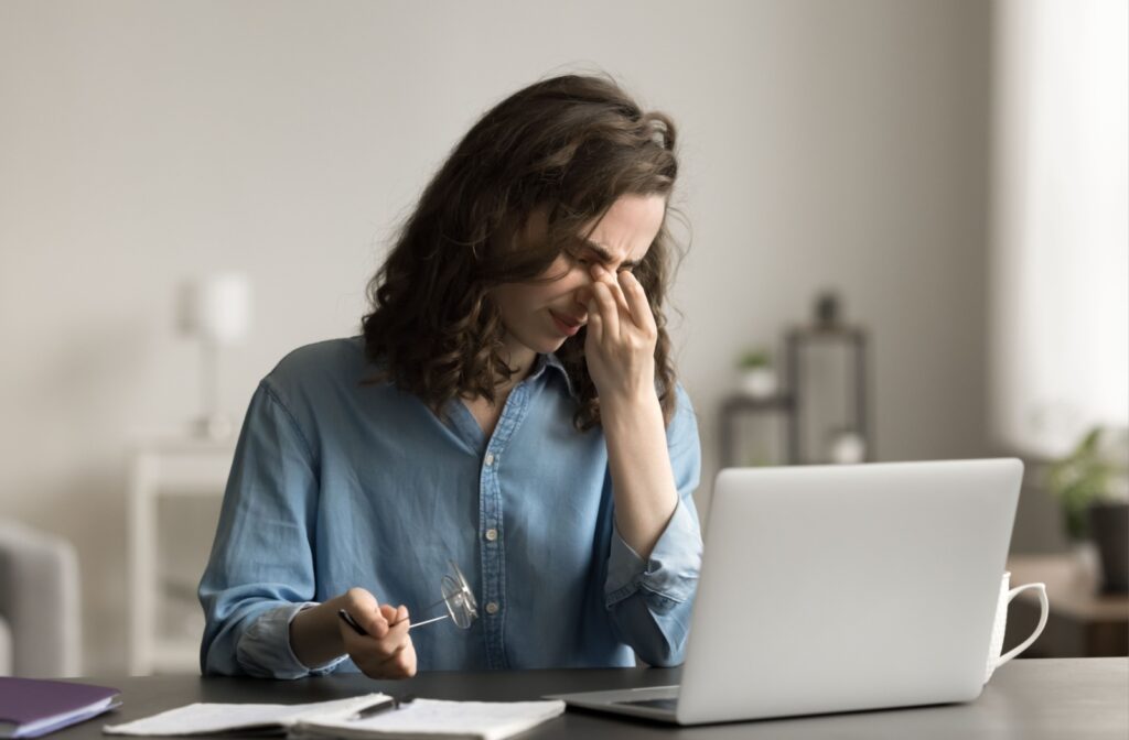 Woman sitting at desk rubbing her eyes from digital eye strain while working on a laptop.