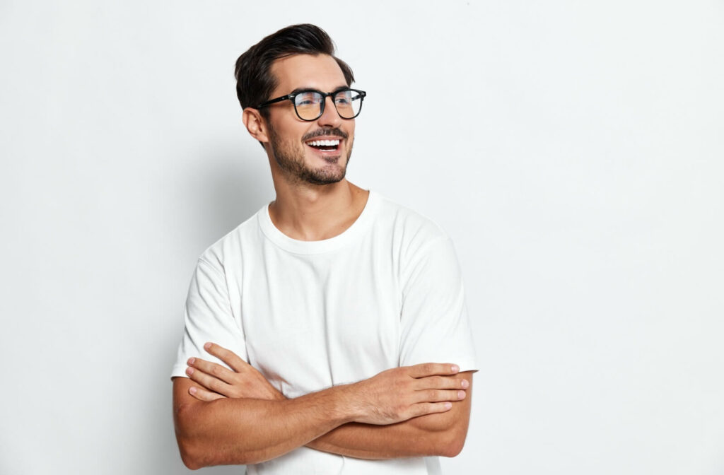 A smiling man with arms crossed wearing modern black-rimmed glasses, showcasing the leading men's eyeglass fashion trends for 2026.