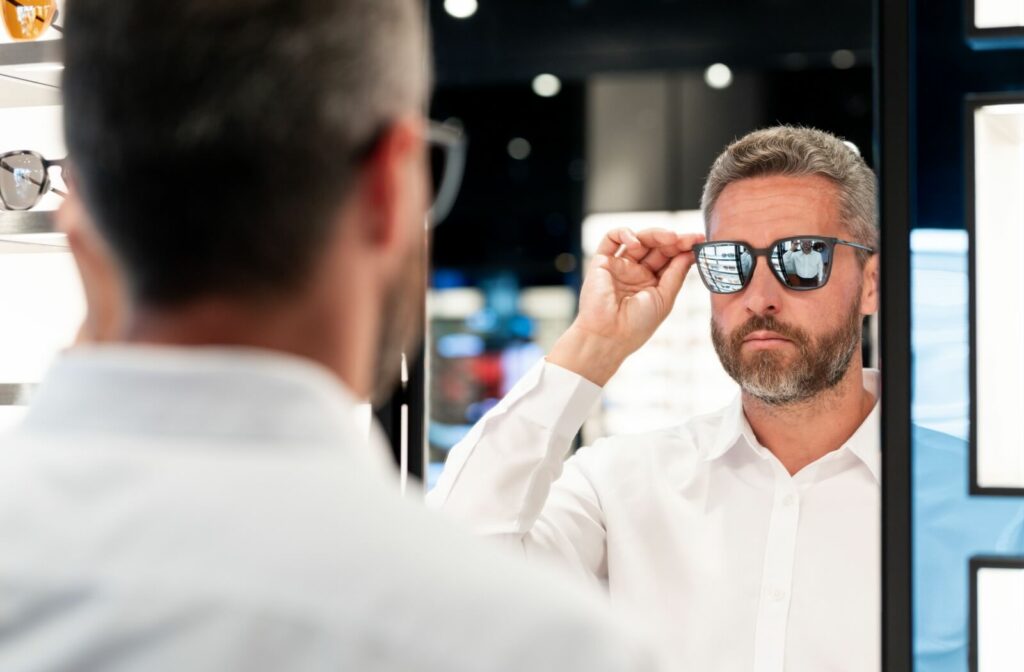 A man looking into an optical store mirror while trying on a pair of dark-rimmed eyeglasses to find the perfect fit.